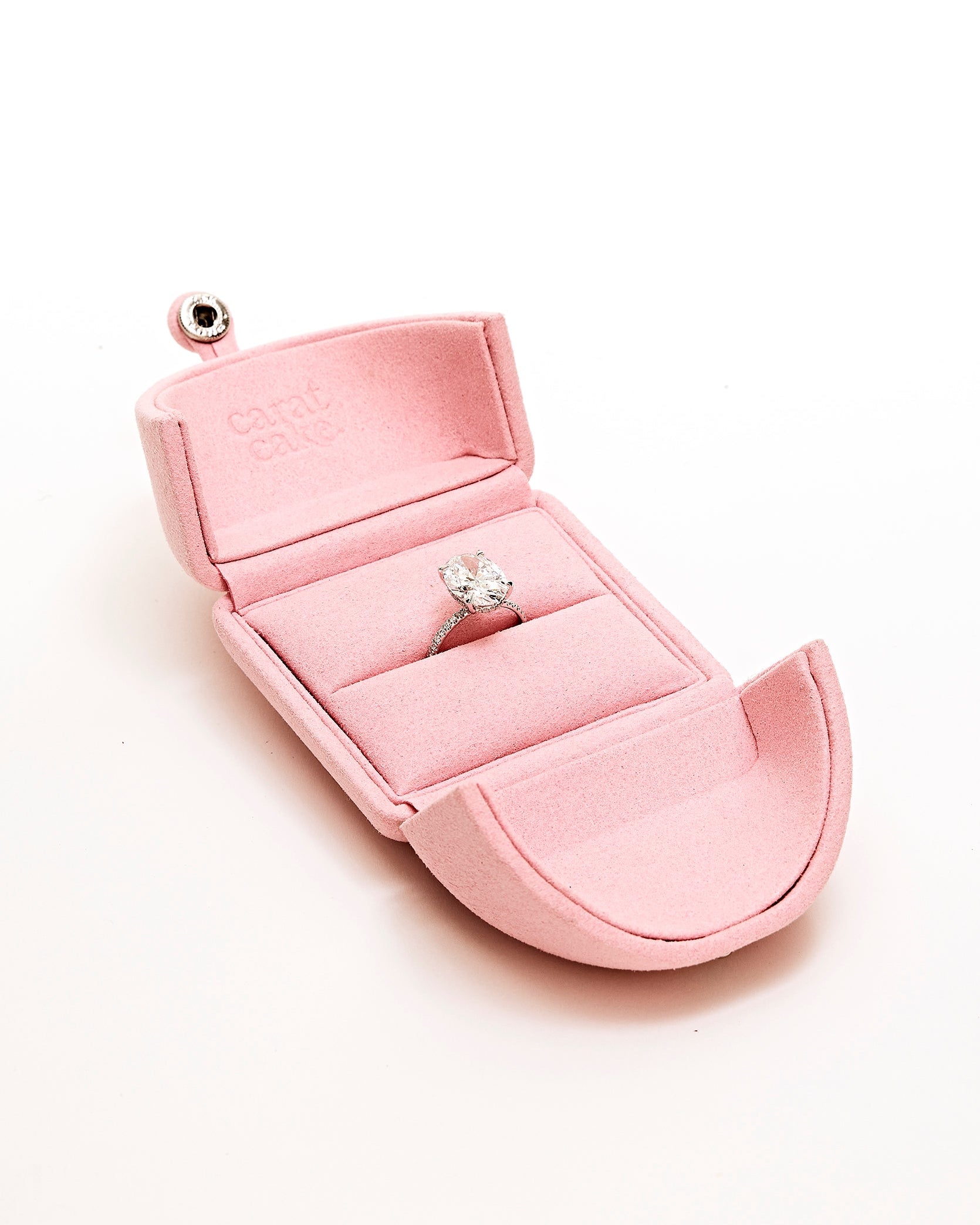 Pink jewelry box with an oval diamond ring inside on a white background