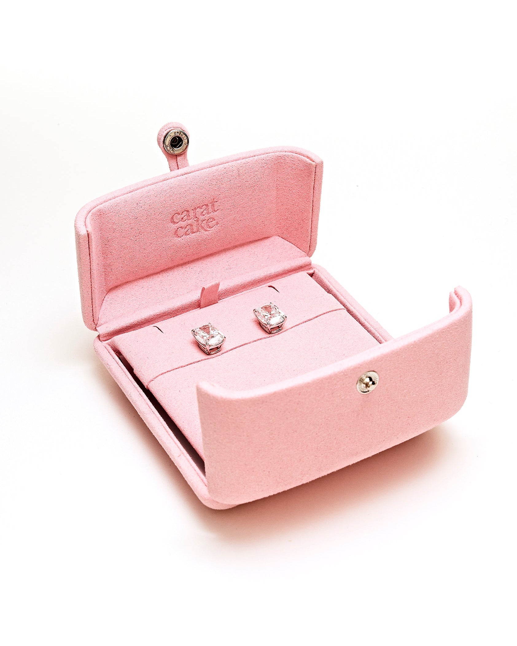 Pink jewelry box with square pair of diamond earrings inside on a white background